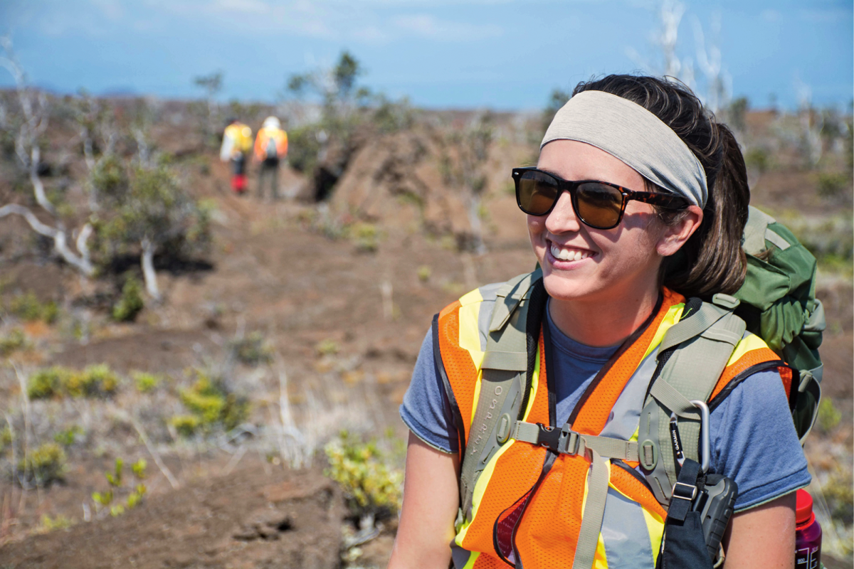 A woman wearing glasses and high-vis gear smiles in an outdoor field